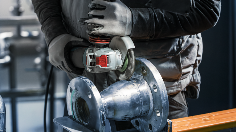 PRO Stainless Steel heavy X-Lock Wire Wheel, 115 x 0.5 mm A person wearing safety equipment grinds a metal pipe with a power tool.