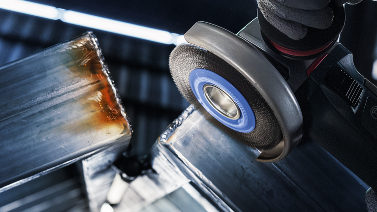 PRO Stainless Steel heavy X-Lock Wire Wheel, 115 x 0.5 mm Person wearing safety equipment grinds the edge of a metal beam.