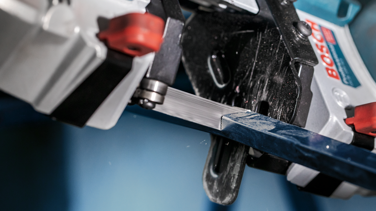 Bandsaw slicing through a metal bar in a close-up industrial setting.