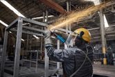A person wearing safety equipment grinds a metal frame, producing bright sparks.