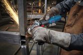 A person wearing safety equipment grinds a steel frame, sparks flying from the contact point.