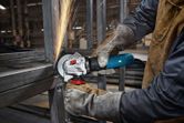 A person wearing safety equipment grinds a metal frame, creating bright sparks.