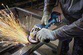 A person wearing safety equipment grinds a metal beam with an angle grinder.