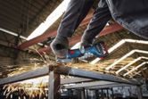A person wearing safety equipment grinds a metal beam with an angle grinder.