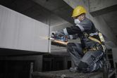 A person wearing safety equipment grinds concrete with a power tool on a construction site.