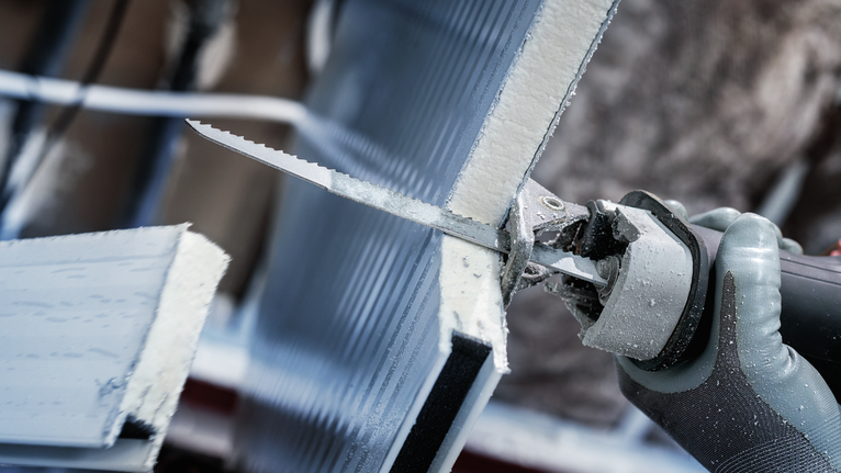 Person wearing safety equipment cutting a foam board with a reciprocating saw.