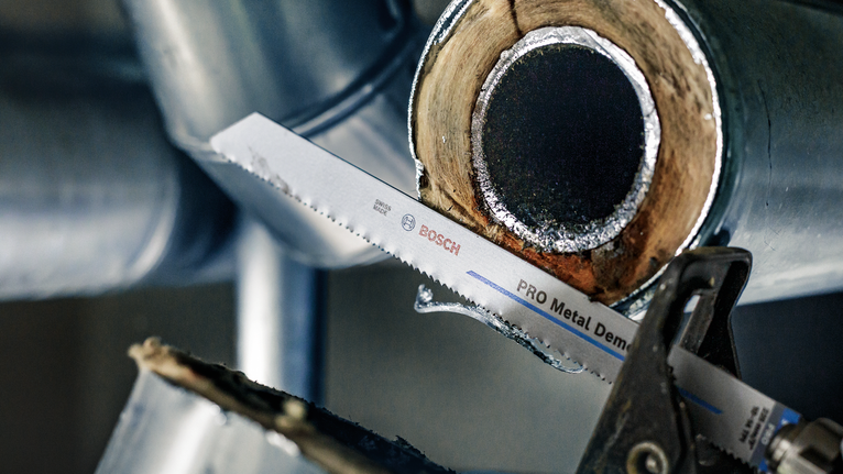Saw blade cutting through a metal pipe in an industrial setting.
