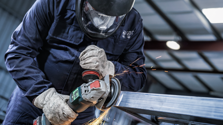 A person wearing safety equipment grinds metal, creating sparks.