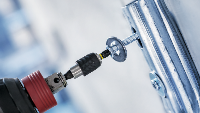 Cordless drill driving a screw into a metal bracket.