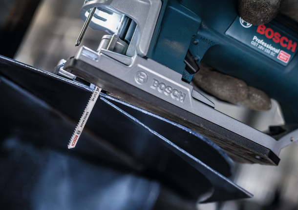 A person wearing safety equipment uses a jigsaw to cut a sheet of metal.