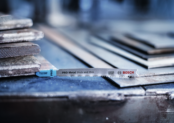 PRO Metal thick and thin T123XF Jigsaw Blade, 100 mm, 5 pcs Jigsaw blade placed on stacked metal sheets in a workshop.