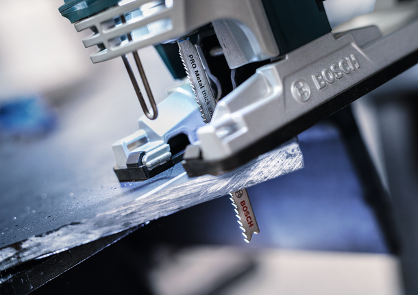 PRO Metal thick and thin T123XF Jigsaw Blade, 100 mm, 5 pcs A jigsaw cutting through a dark metal sheet in a workshop.