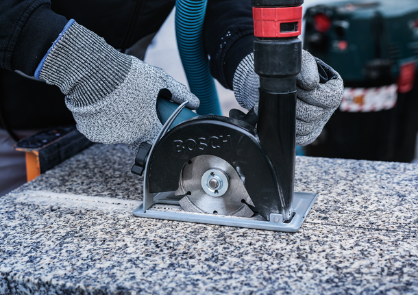 Person wearing safety equipment uses a circular saw to cut a stone surface.