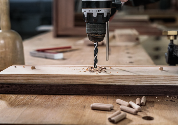 PRO Wood Brad Point Drill Bit Set, 8 pcs A person uses a power drill to make a hole in a wooden board on a workbench.