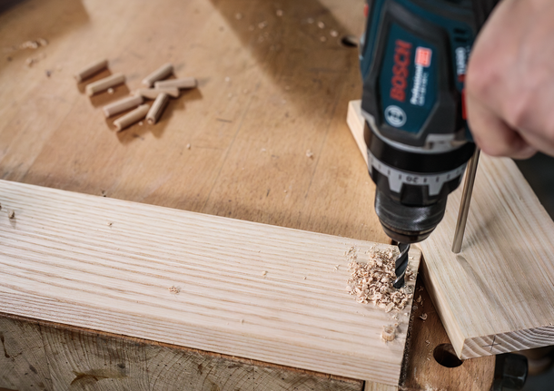 PRO Wood Brad Point Drill Bit Set, 8 pcs Person using a power drill to make a hole in a wooden plank on a workbench.