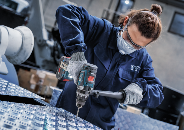 Person wearing safety equipment drills into a metal surface.