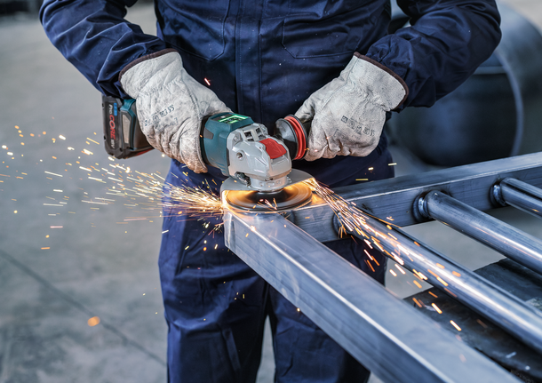 PRO Backing Pad Soft, 125 mm, X-Lock Person wearing safety equipment grinds a metal frame with an angle grinder, producing sparks.