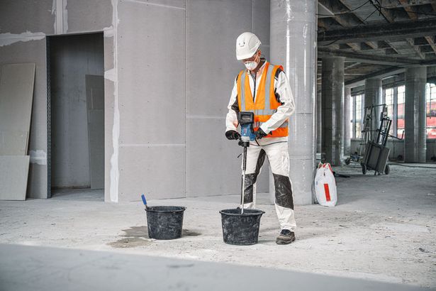 GRW 18V-120 A person wearing safety equipment uses a stirring mechanism to mix material in a bucket.