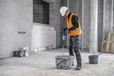 A person wearing safety equipment mixes material with a stirring mechanism on a construction site.