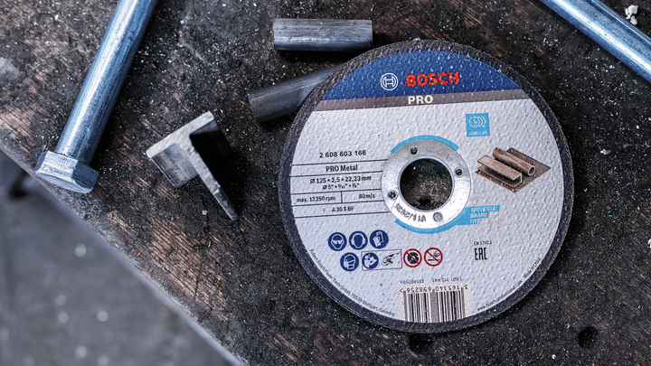 Object #200483037: 3089912_app_web_7 Cutting disc for metal work placed on a rough workbench beside bolts and metal pieces.