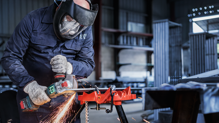 Person wearing safety equipment uses a power tool to grind metal, creating sparks.