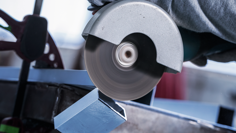 Worker wearing safety equipment uses a circular saw to cut a metal beam.