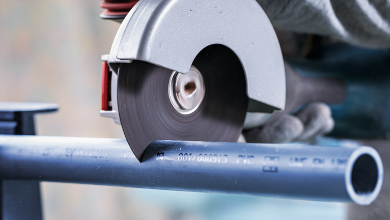 Circular saw cutting a blue plastic pipe, worker wearing safety equipment.