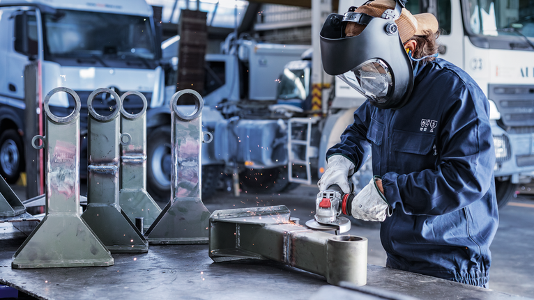 PRO Metal Bonded Grinding Disc, 125 x 6 x 22.23 mm, X-Lock Person wearing safety equipment grinds a metal part in an industrial setting.
