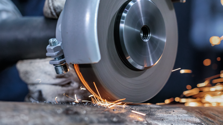 A person wearing safety equipment grinds metal with a power tool, producing sparks.