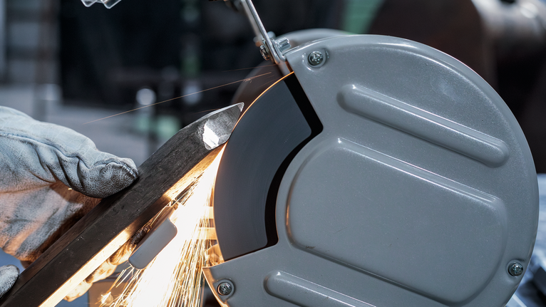PRO Metal Grinding Wheel, 200 x 25 x 32 mm, G46 A person wearing safety equipment grinds a metal bar with a bench grinder.