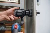 A person operates a cordless hydraulic punching tool on a metal panel.