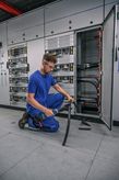 A person wearing safety equipment cuts a thick cable in front of an open electrical panel.
