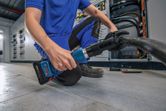 A person wearing safety equipment uses a cordless hydraulic cutting tool on a thick cable.