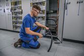 A person wearing safety equipment uses a cordless hydraulic cutting tool on a thick cable.