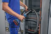 A person wearing safety equipment uses a cordless hydraulic cutting tool on thick cables.