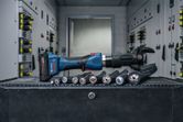 Cordless hydraulic cutting tool placed on a workbench beside thick electrical cables.