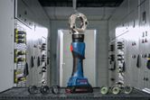 Cordless hydraulic crimping tool with interchangeable dies on a workbench in an electrical room.