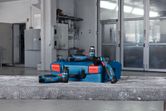 Cordless random orbit sanders and a blue case placed on a concrete surface in a workshop.
