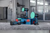 Three cordless polishers with green pads are placed on a blue case in a workshop.