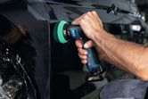 A person uses a cordless polisher to buff the surface of a black car door.