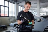 A person wearing safety equipment applies polish to a power polisher in an auto workshop.