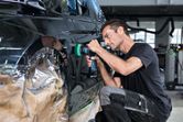 A person wearing safety equipment polishes a car door with a cordless tool.