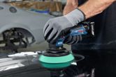 A person wearing safety equipment polishes a car surface with a cordless polisher.