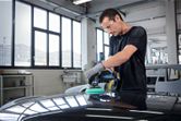 A person wearing safety equipment polishes a car hood with a cordless polisher.