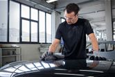 A person wearing safety equipment polishes a car hood with a cloth in a workshop.