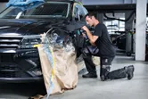 A person wearing safety equipment polishes a car fender in an auto workshop.