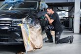 A person wearing safety equipment polishes a car fender in an auto workshop.