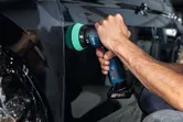 A person polishes a black car door using a cordless polisher.
