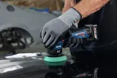 A person wearing safety equipment polishes a car surface with a cordless polisher.