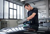 A person wearing safety equipment polishes a car hood in an auto workshop.